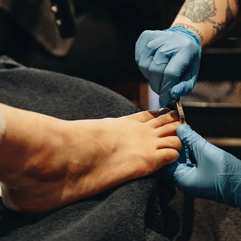 Pedicure nail tech using tool for a clients cuticles on their feet